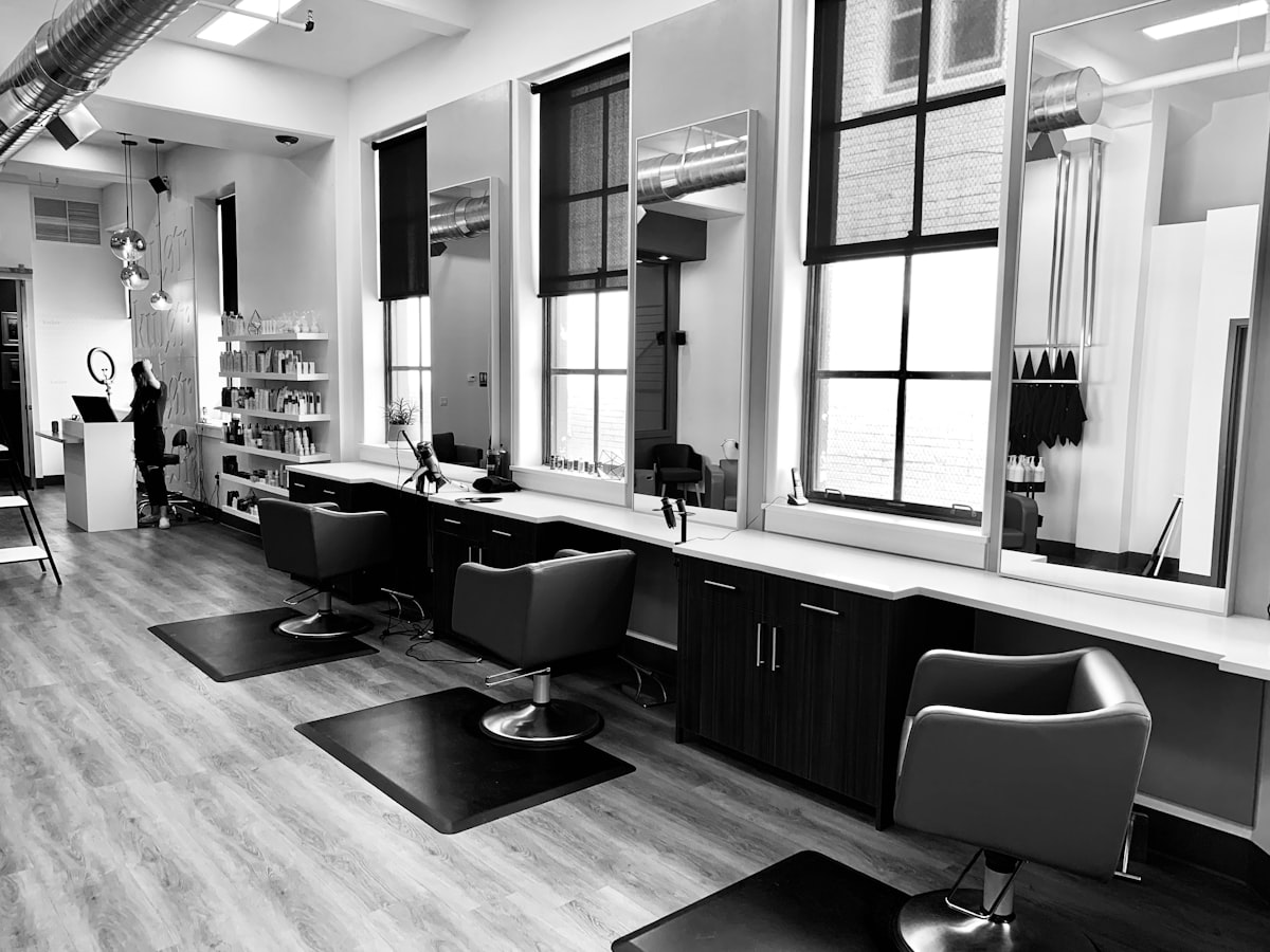 Elena's Hair Studio – eleganter Salon-Innenraum mit Logo auf Milchglaswand, goldene Spiegel und beige Polsterstühle